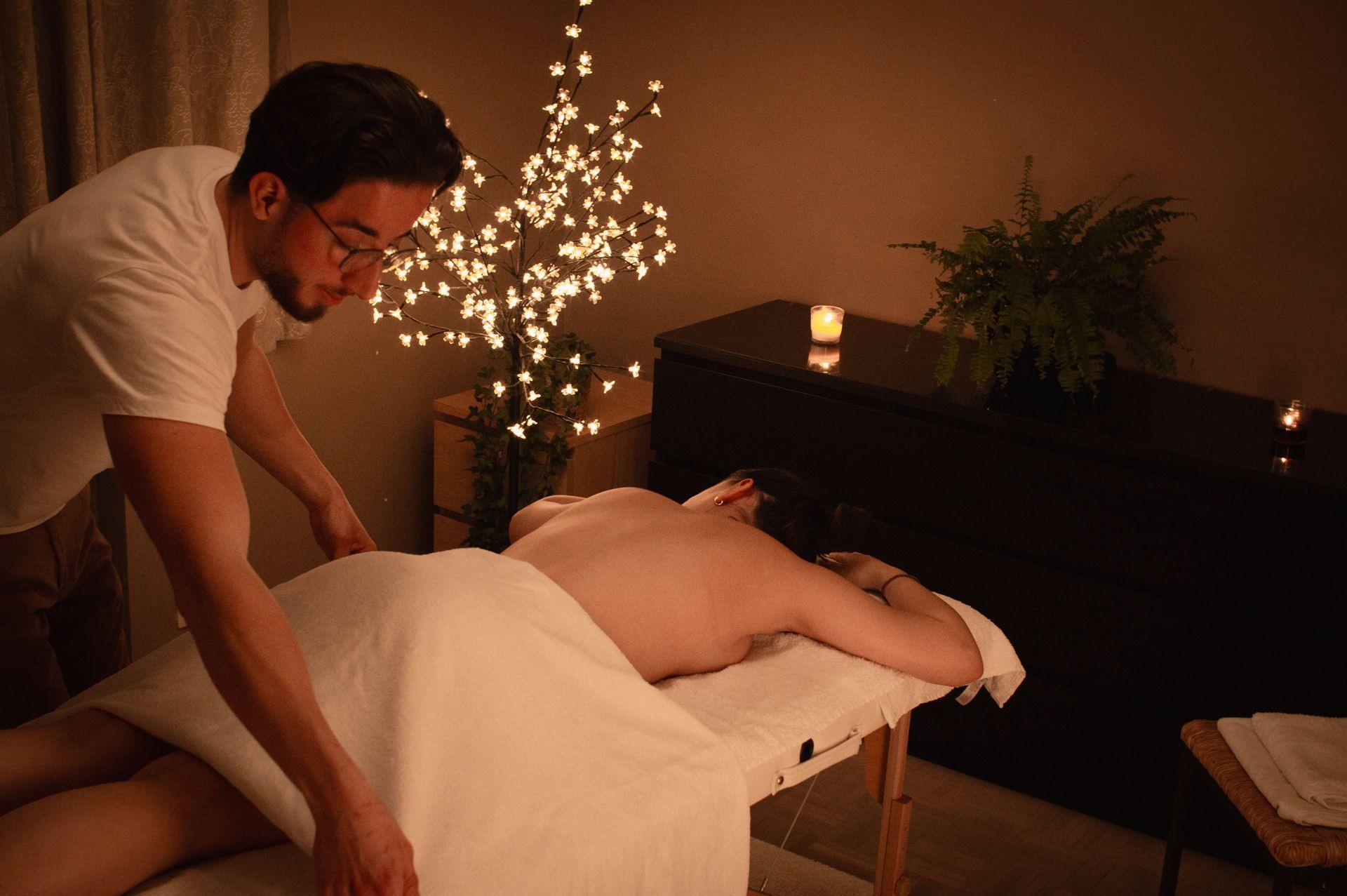 Person receiving a massage in a dimly lit room with candles and a decorative lighted tree.